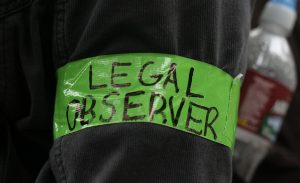 A green band reading: "legal observer" can be seen on someone's arm.