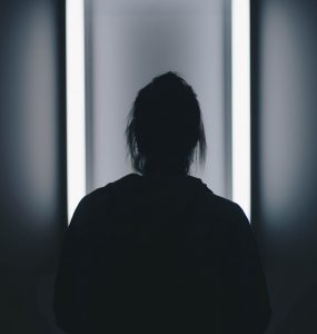 A woman's silhouette can be seen standing infront of a bright mirror.