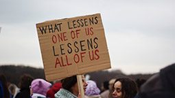 placard saying 'what lessens one of us lessens all of us'