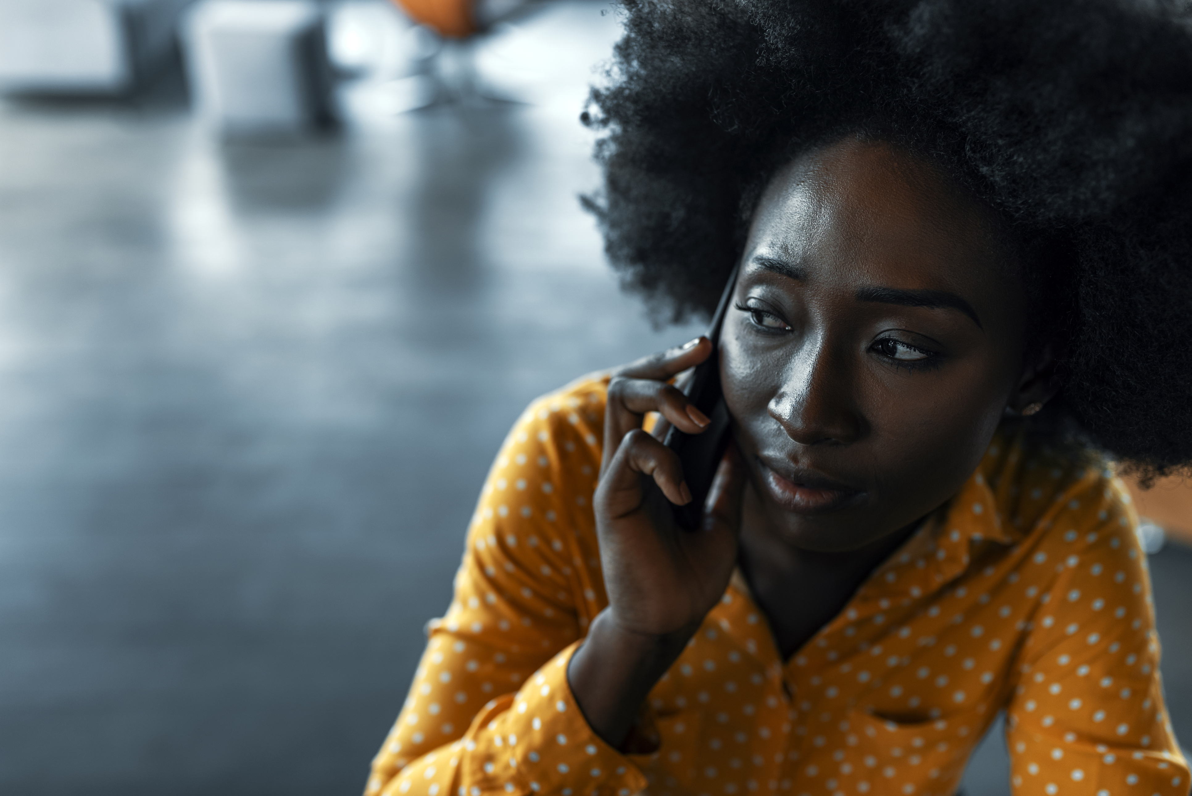 Young black woman in yellow shirt with anxious expression on her phone.