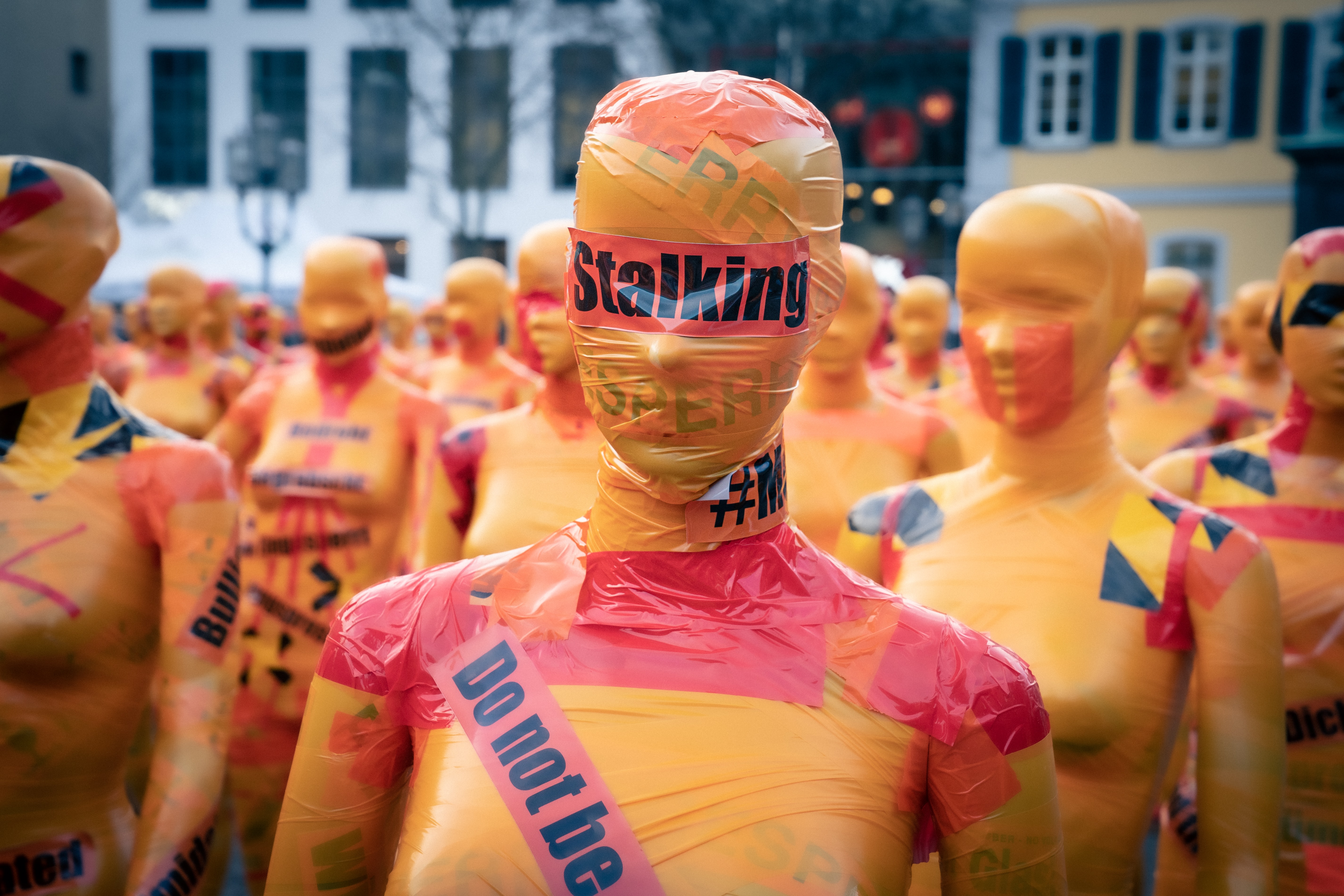 In an artistic demonstration, a series of female dummies are covered with tape with various crimes written across their faces on black tape. This doll has "stalking" across the eyes on red tape. 
