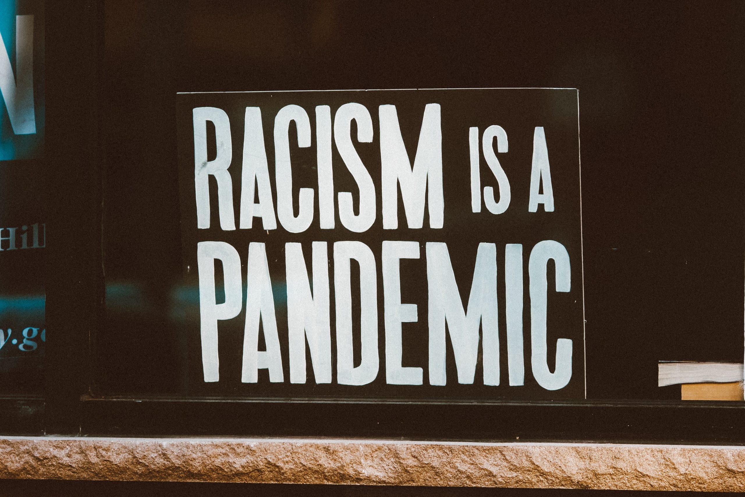 A sign in a widnow reads "Racism is a pandemic" in white lettering on a black background. 
