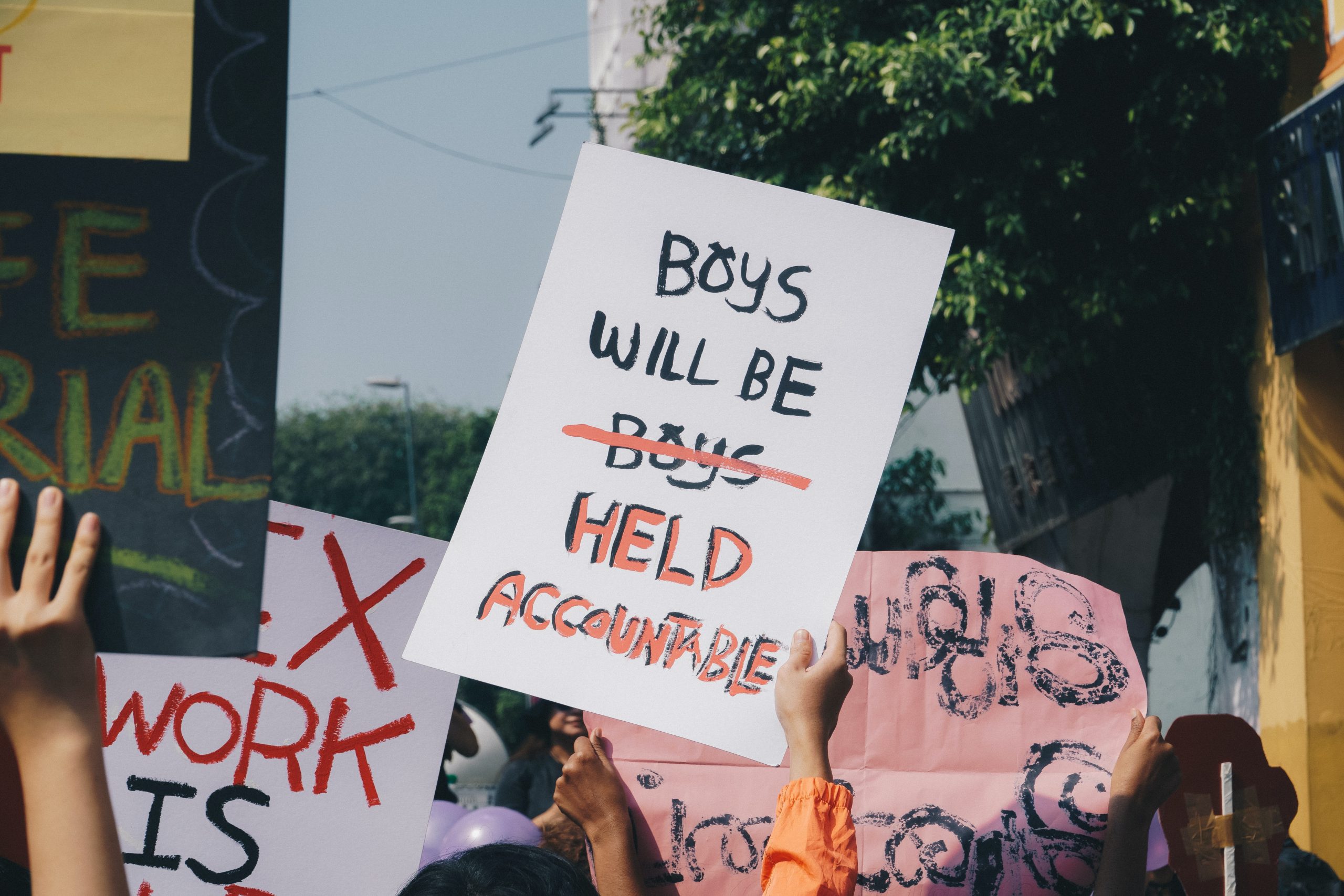 A woman holds a sign above a crowd that reads "boys will be held accountable"
