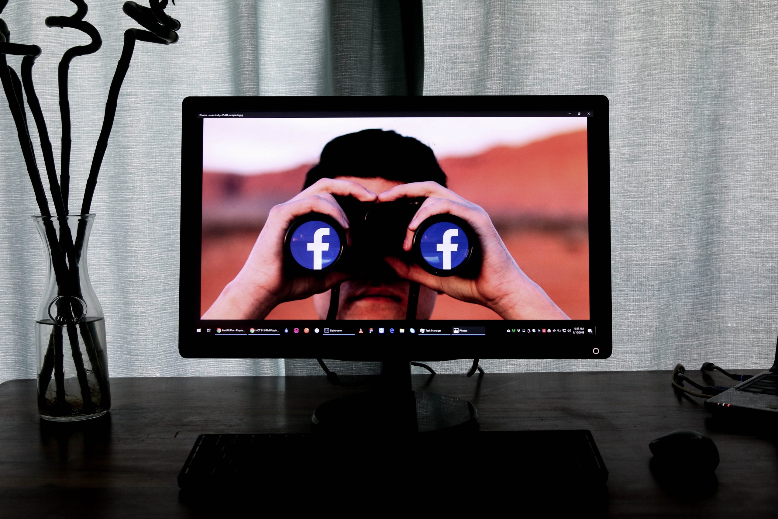 A computer screen shows a man using a pair of binoculars looking at the photographer. The Facebook logo is shown in both the eye holes.
