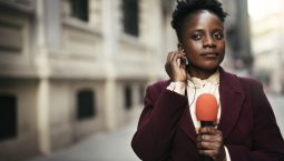 African female news reporter in live broadcasting. TV reporter presenting the news outdoors.
