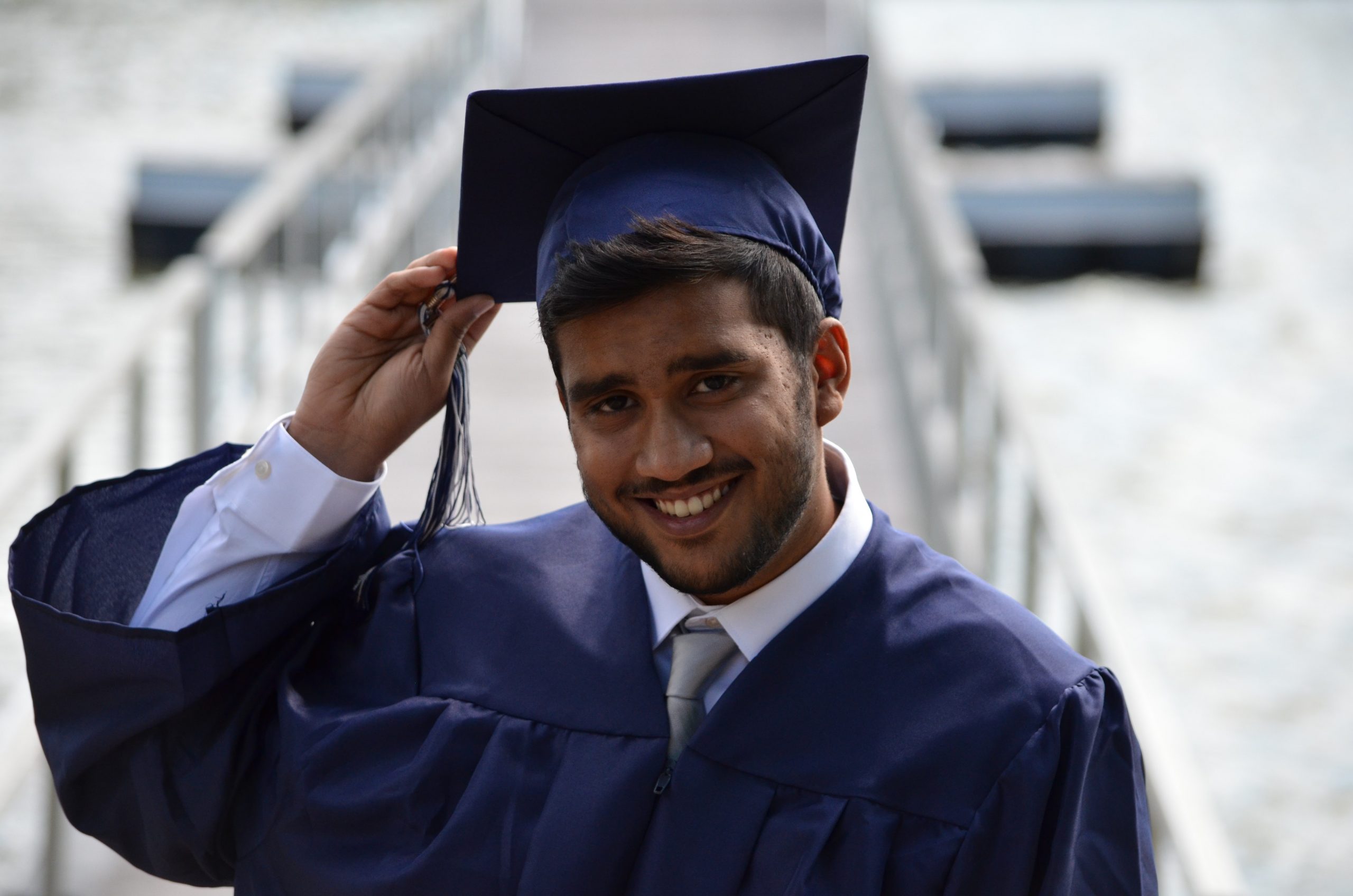 A young south Asian man wears a cap and gown and smiles at the camera.