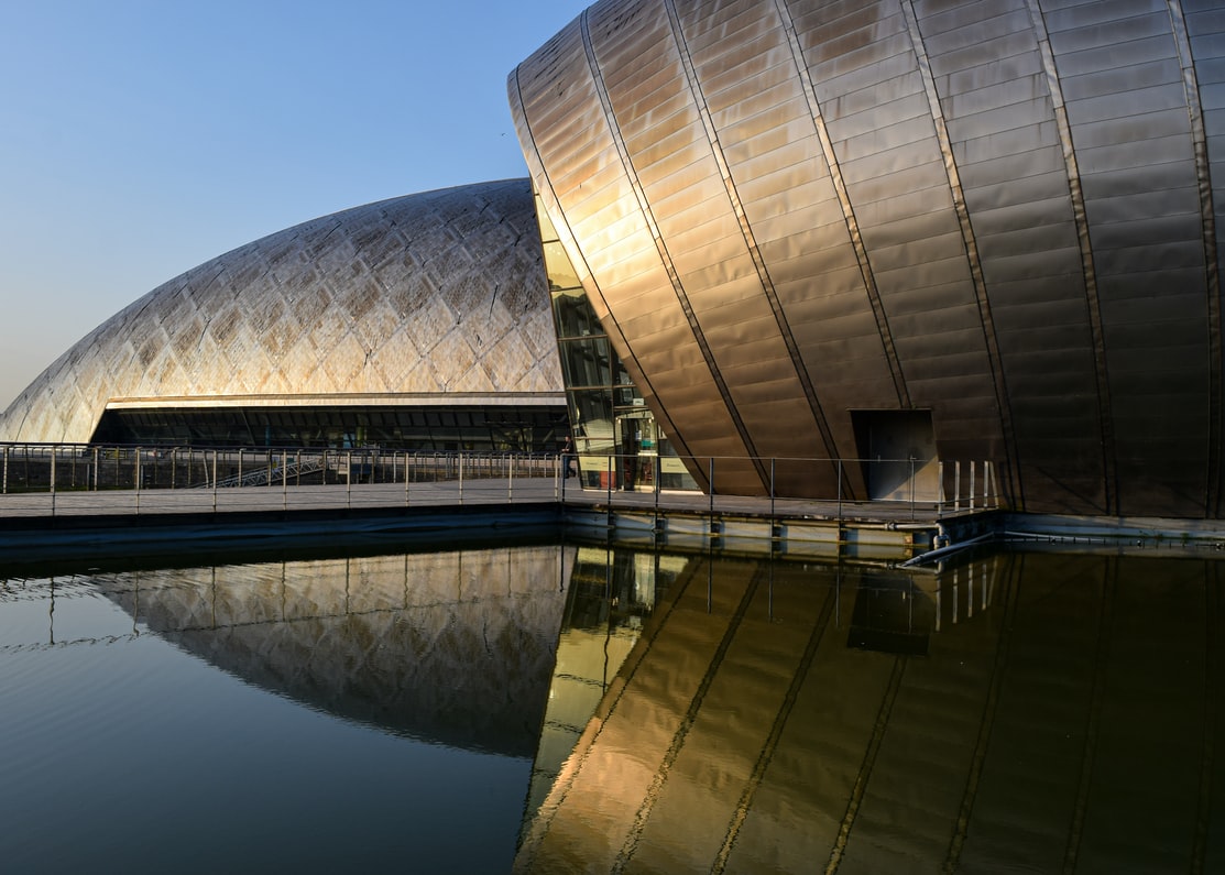 A photo of Glasgow Science Centre in the sunshine and its reflection in an adjacent pool