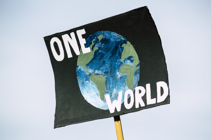 A placard depicts the Earth in blue and green against a black space backdrop with the words 'One World' written besides it in white