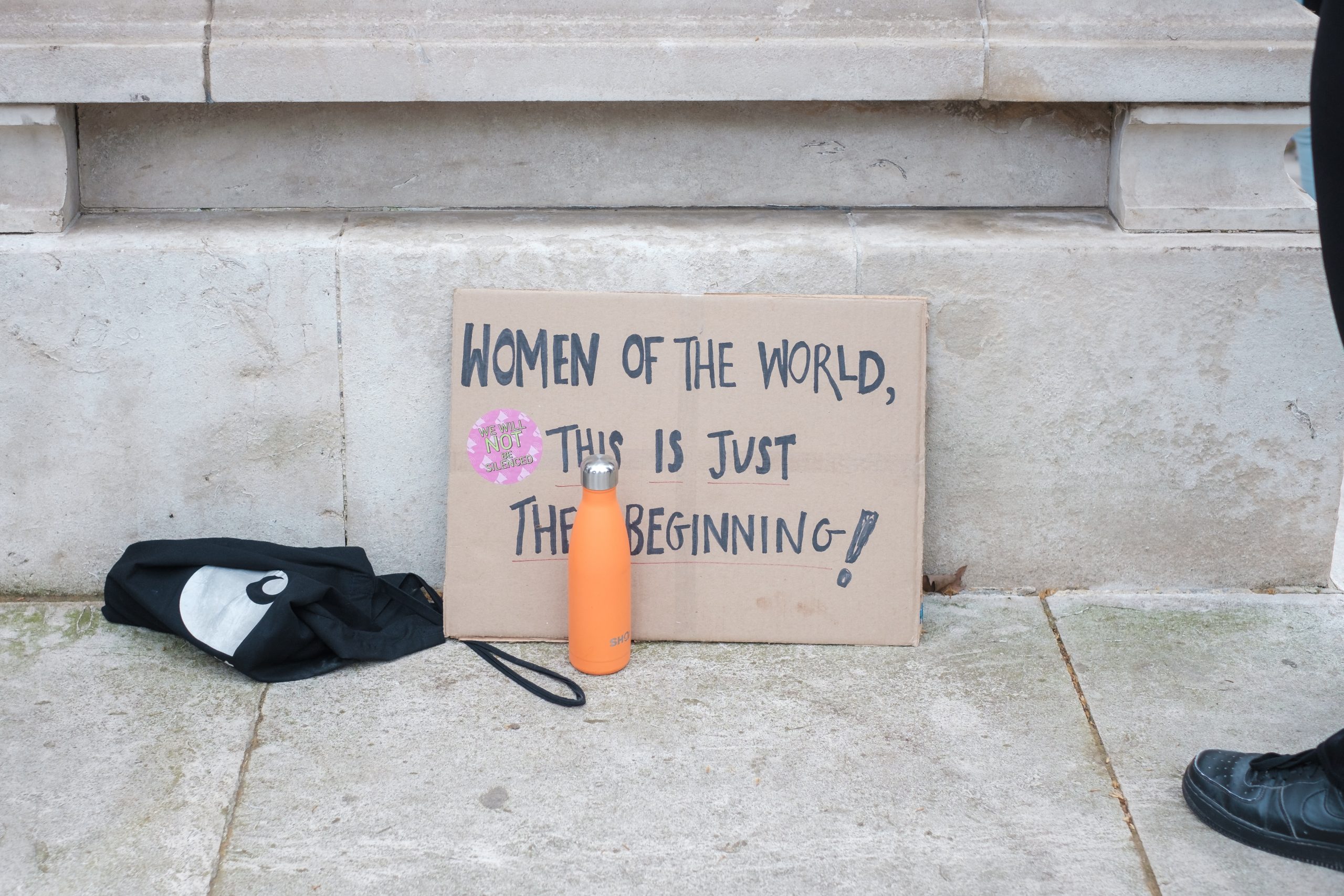 A sign leaning against a stone wall on the floor reads "women of the world, this is just the beginning"