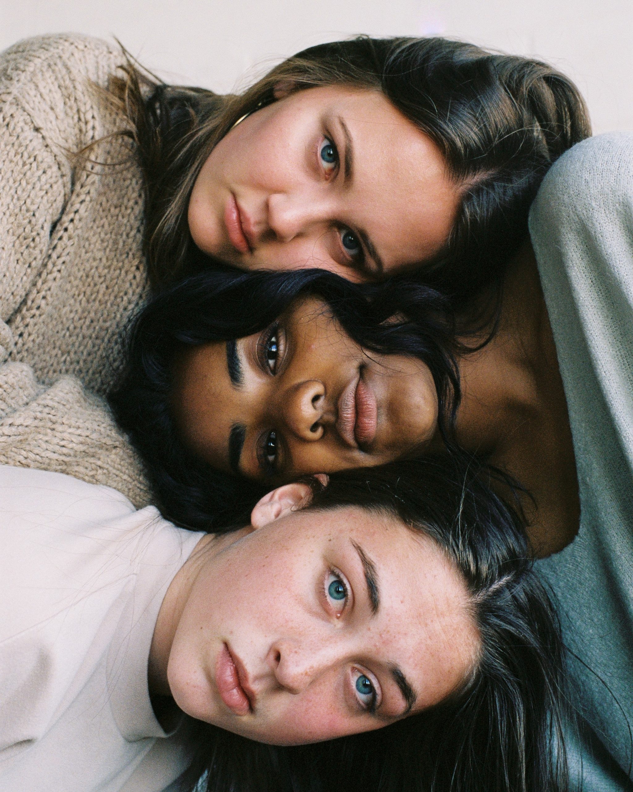 A trio of girls look a the camera. Their heads are stacked on top of each other. 