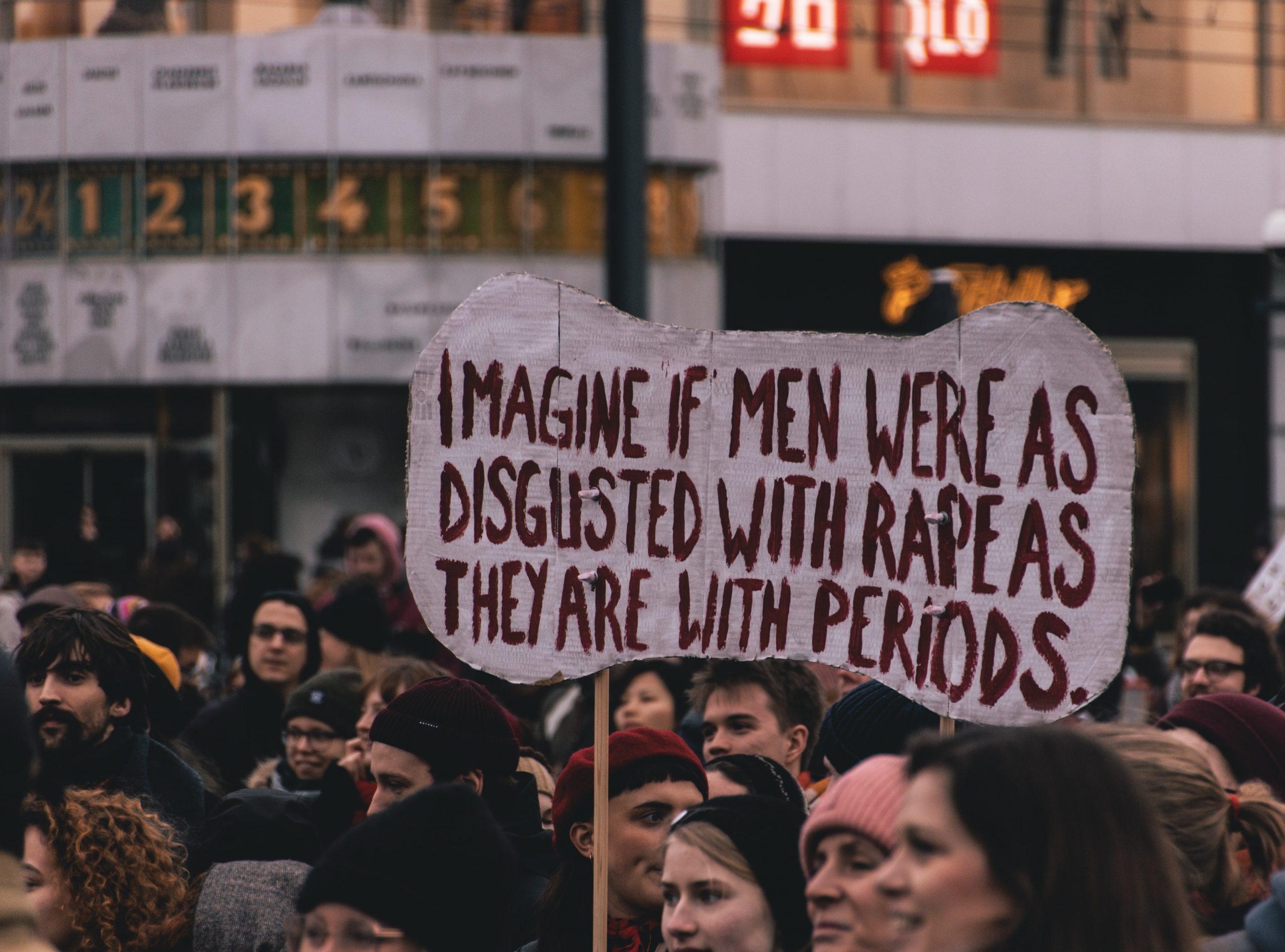 A sign in red lettering reads "imagine if men were as disgusted with rape as they are about periods"