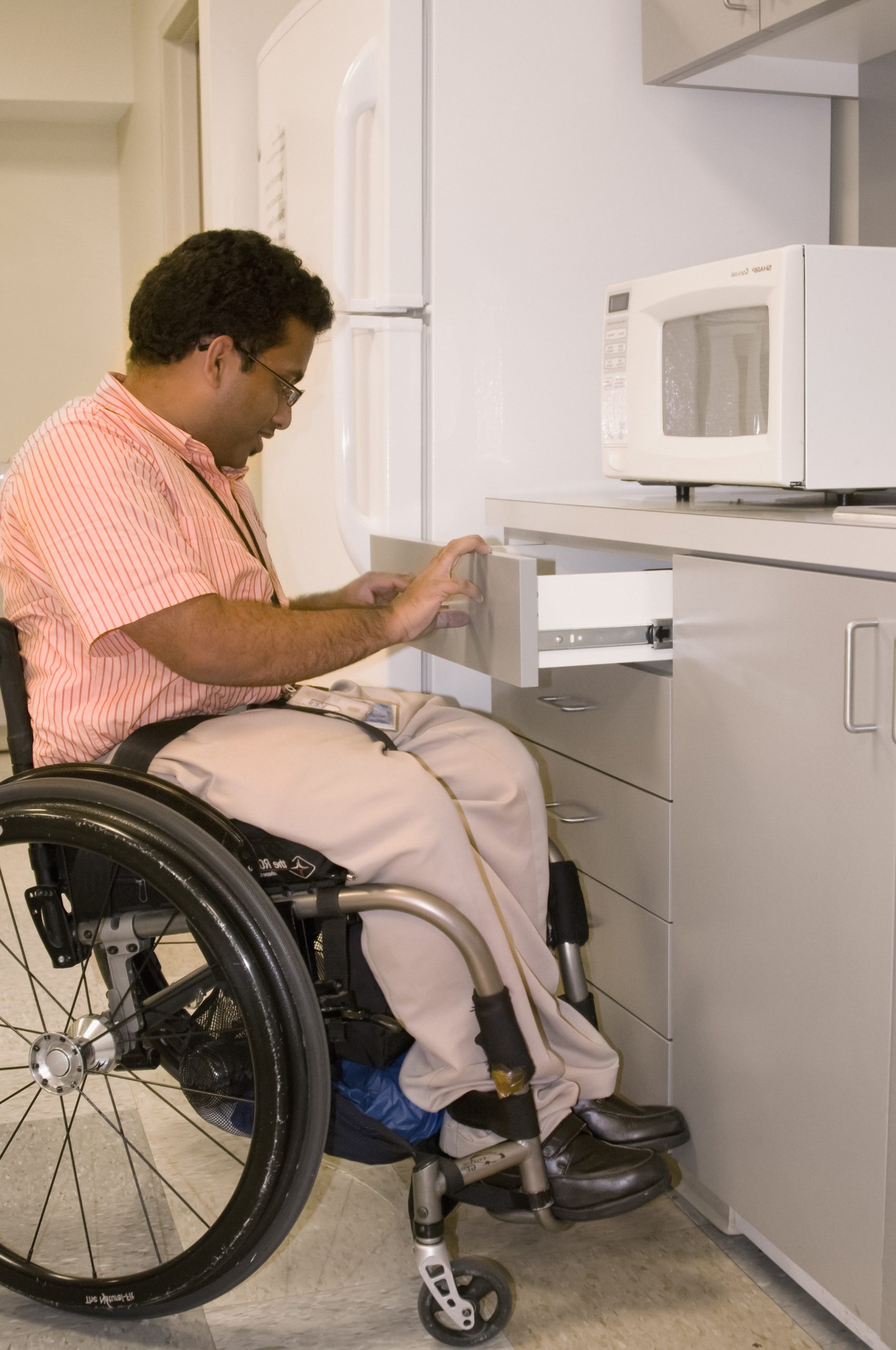 A man using a wheelchair opens a drawer in a kitchen