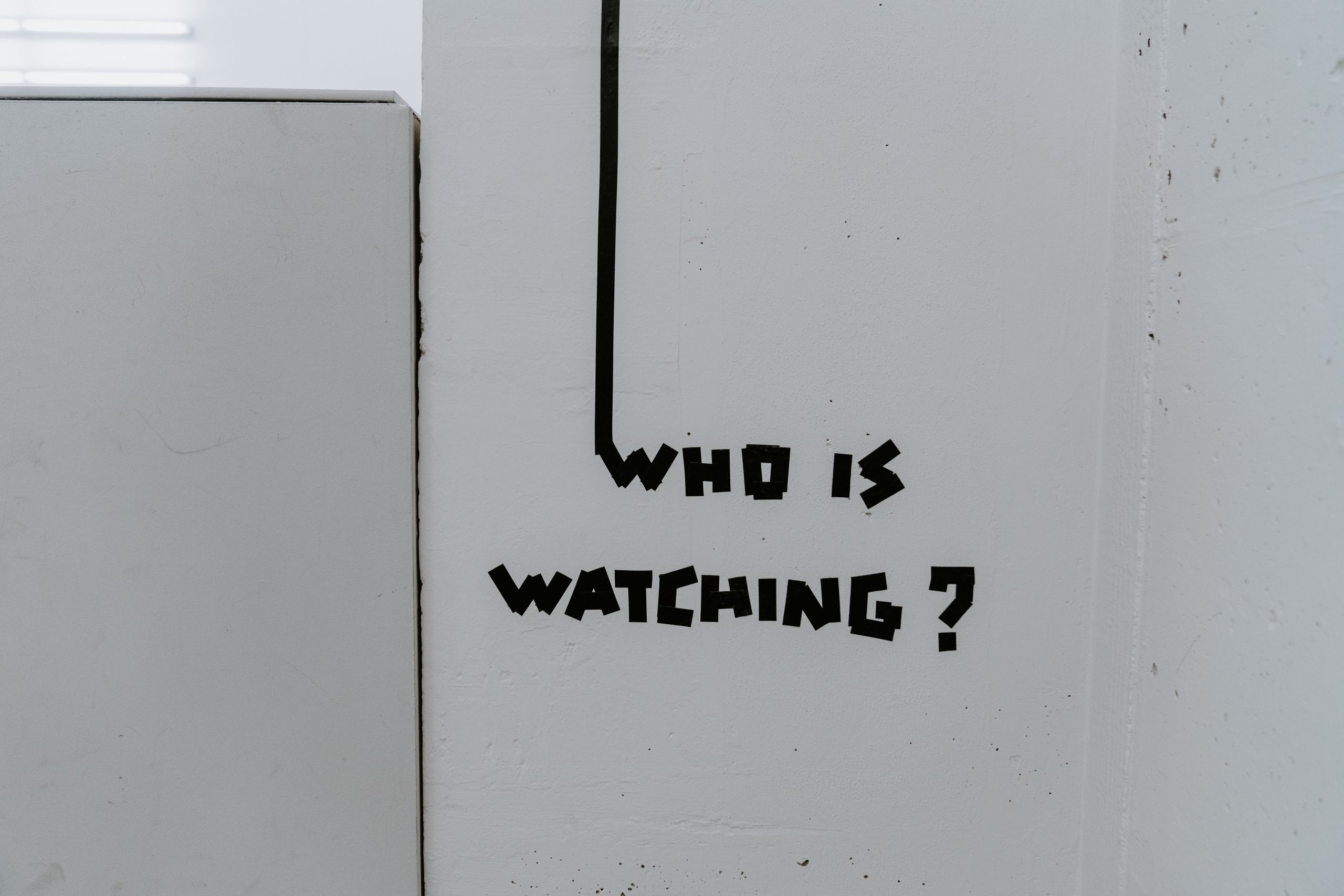 A white wall shows "Who is watching?" written in black ape.