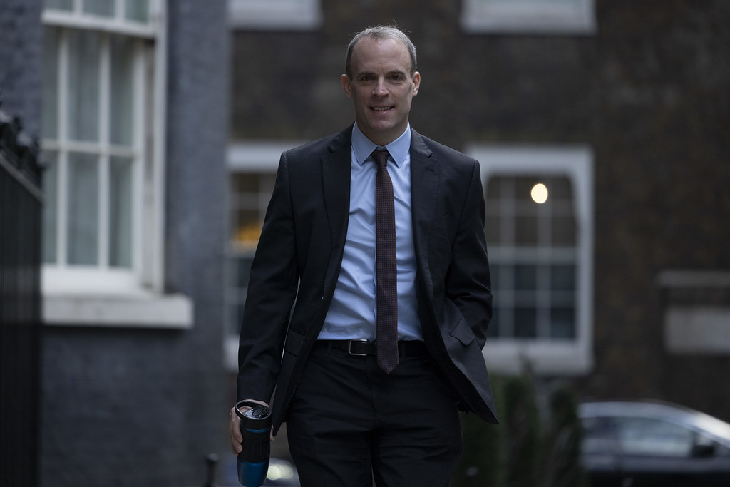 Dominic Raab is pictured in a black suit and tie walking down the street with his hands in his pockets