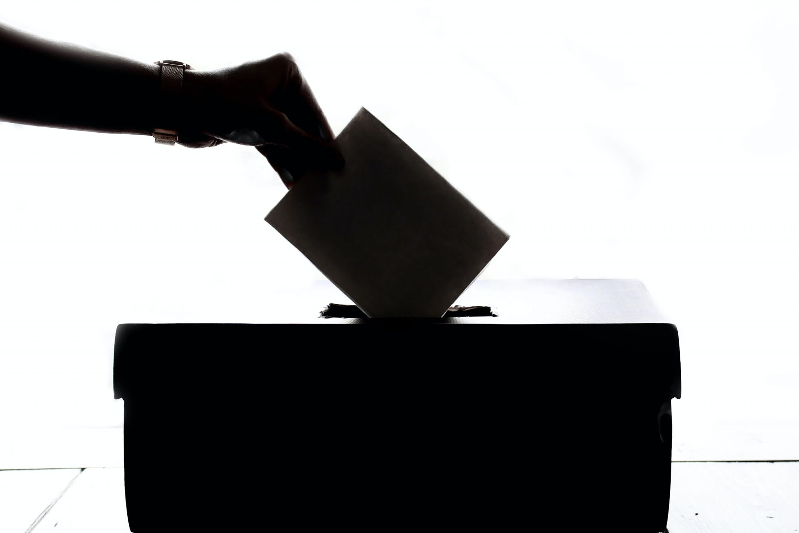 A silhouetted hand posts a vote into a ballot box