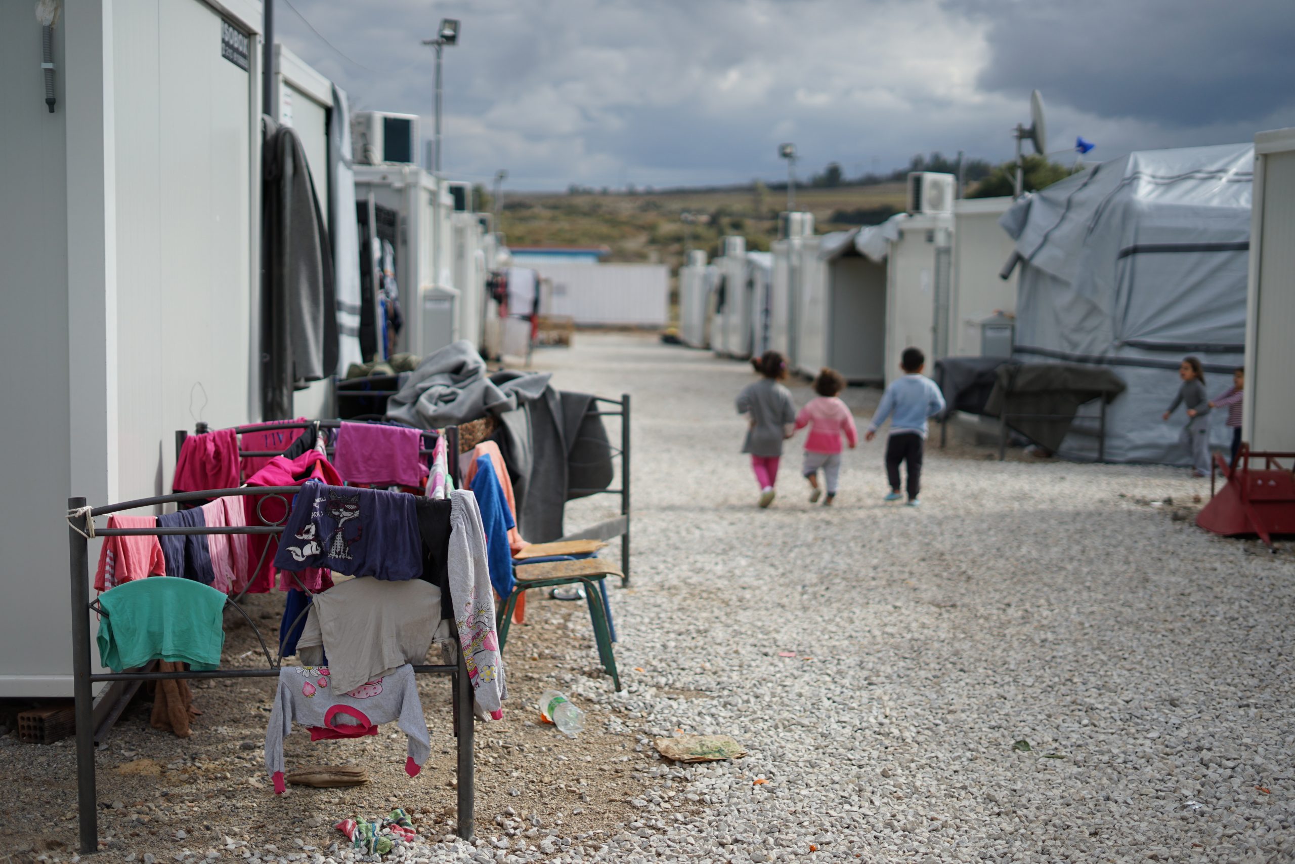 The photo shows a refugee camp with three small children walking in the distance