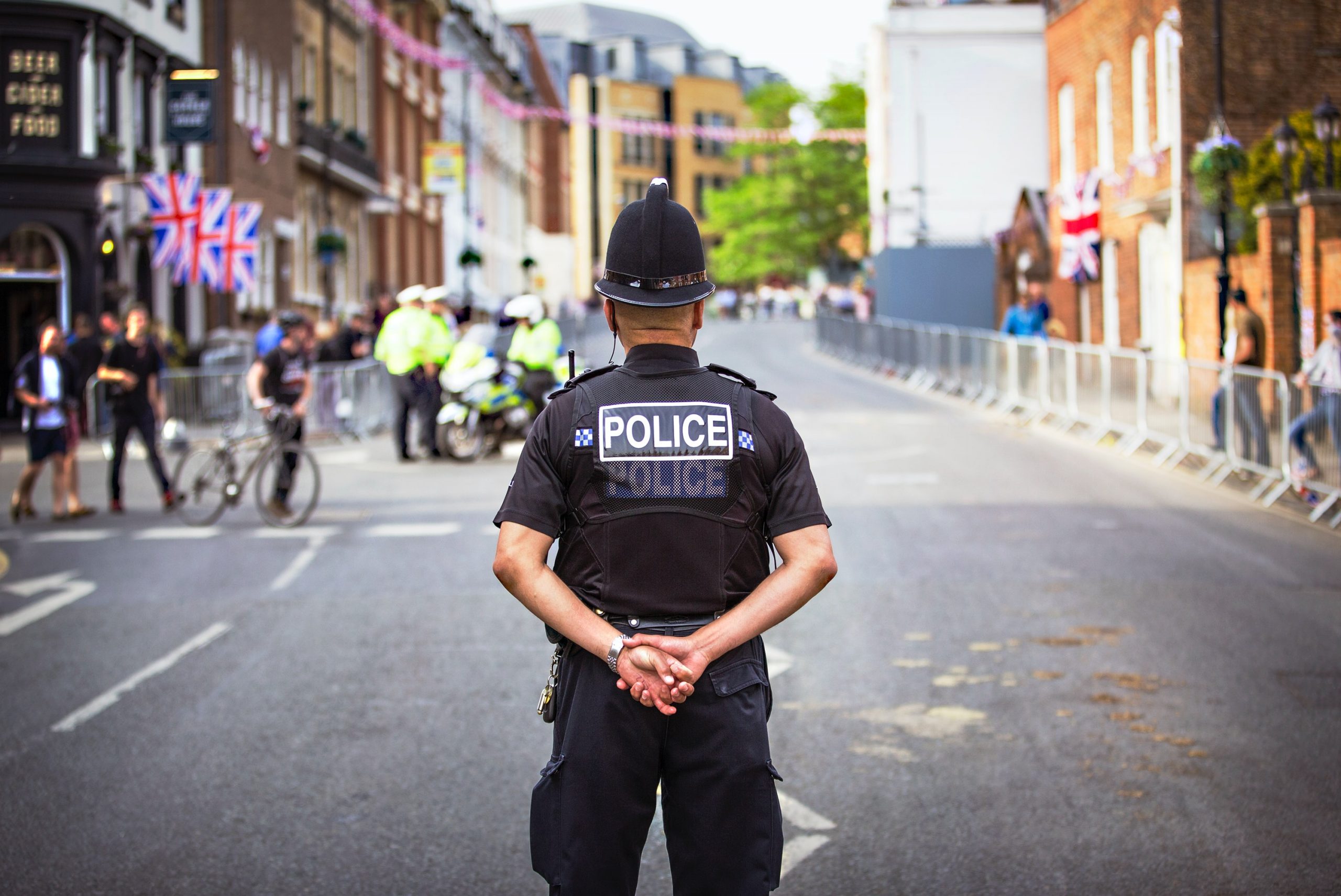 A UK police officer looks out into a road with his hands crossed behind his back