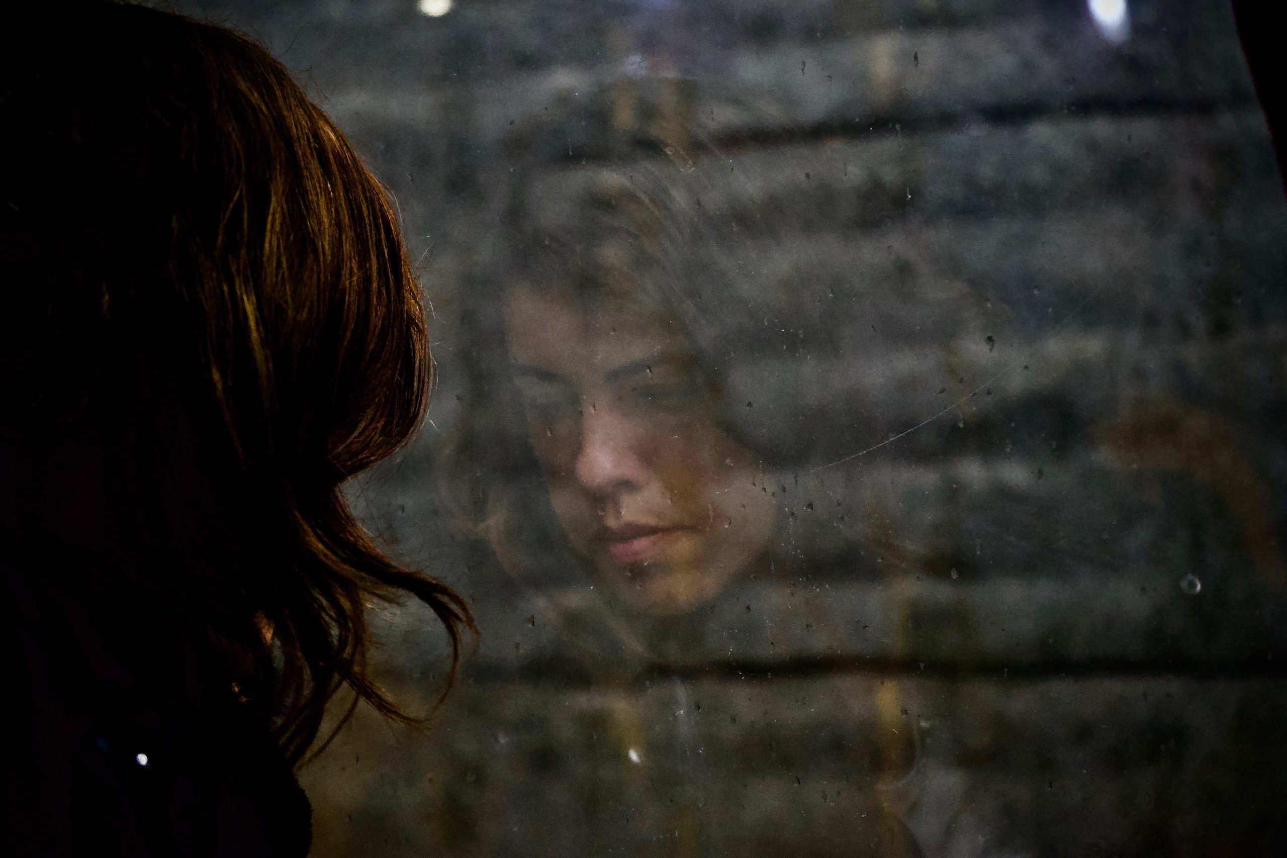 A young person's reflection is shown in a window. They look saddened