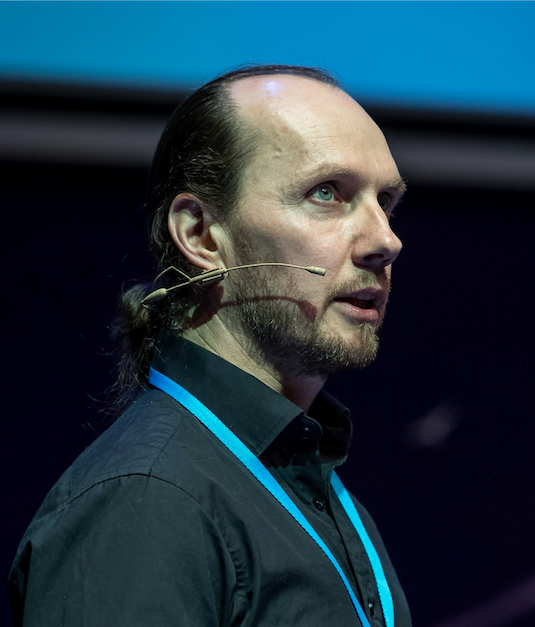 Kemal Pervanic gives a talk using a head-worn microphone in a black shirt with a blue lanyard.