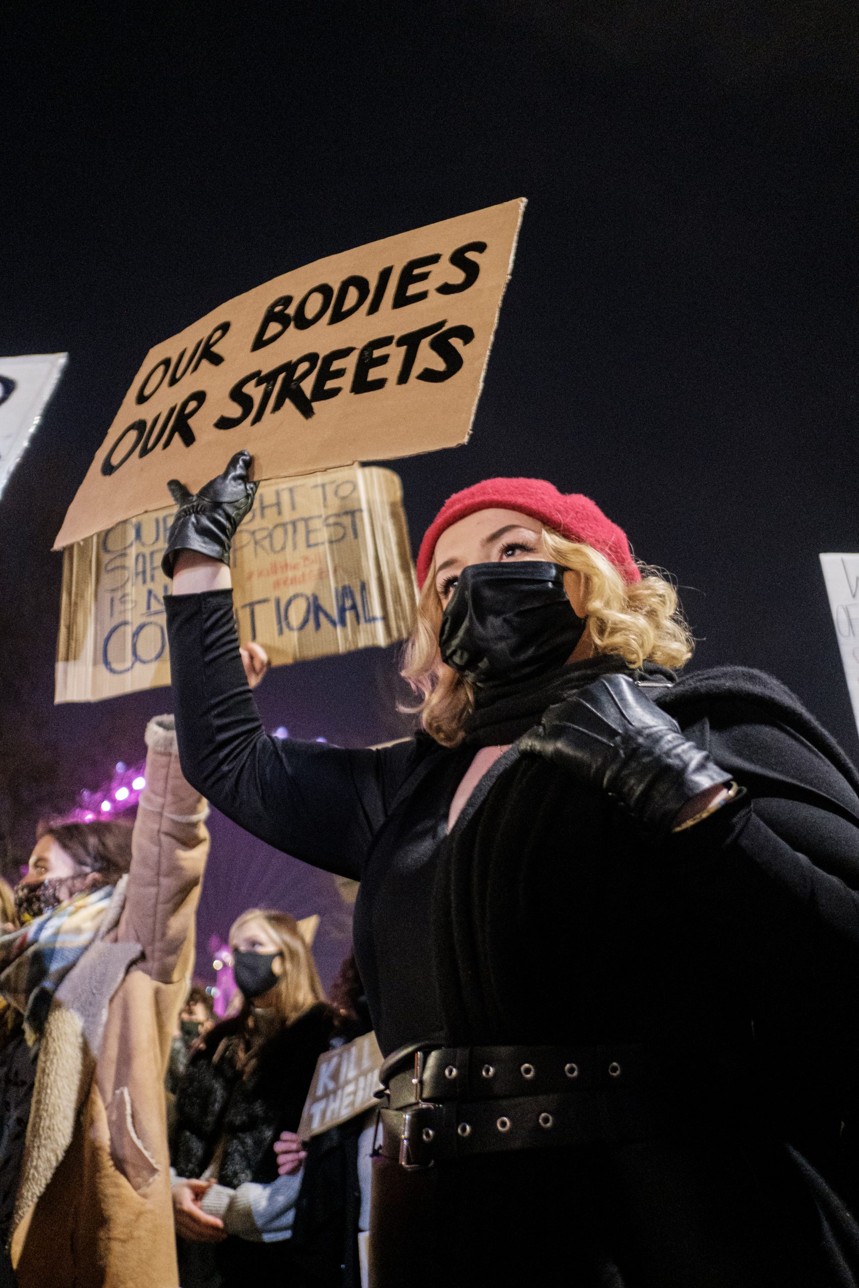 A protester at a vigil holds a sign that reads "our bodies our streets" in black capital letters
