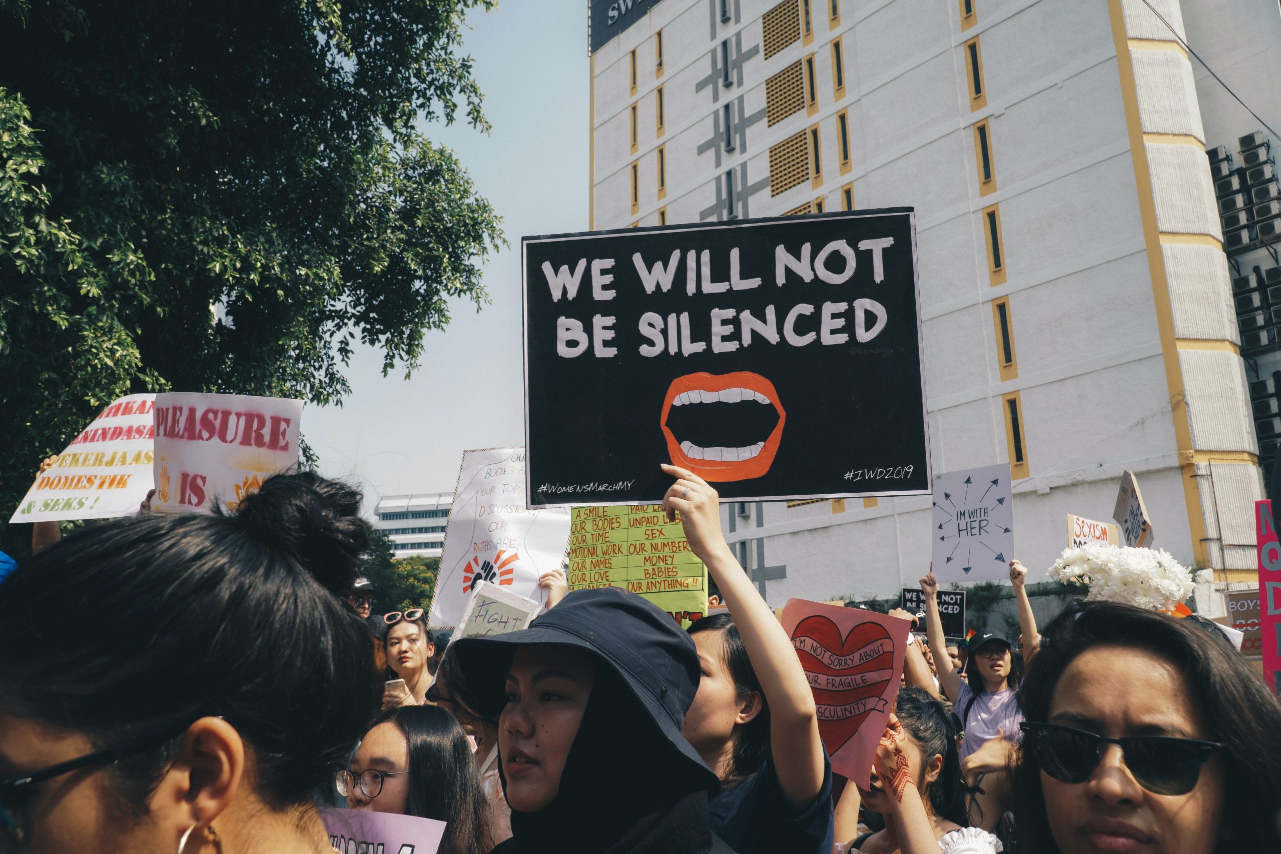 A sign held above a crowd reads "we will not be silenced" at a women's rights protest