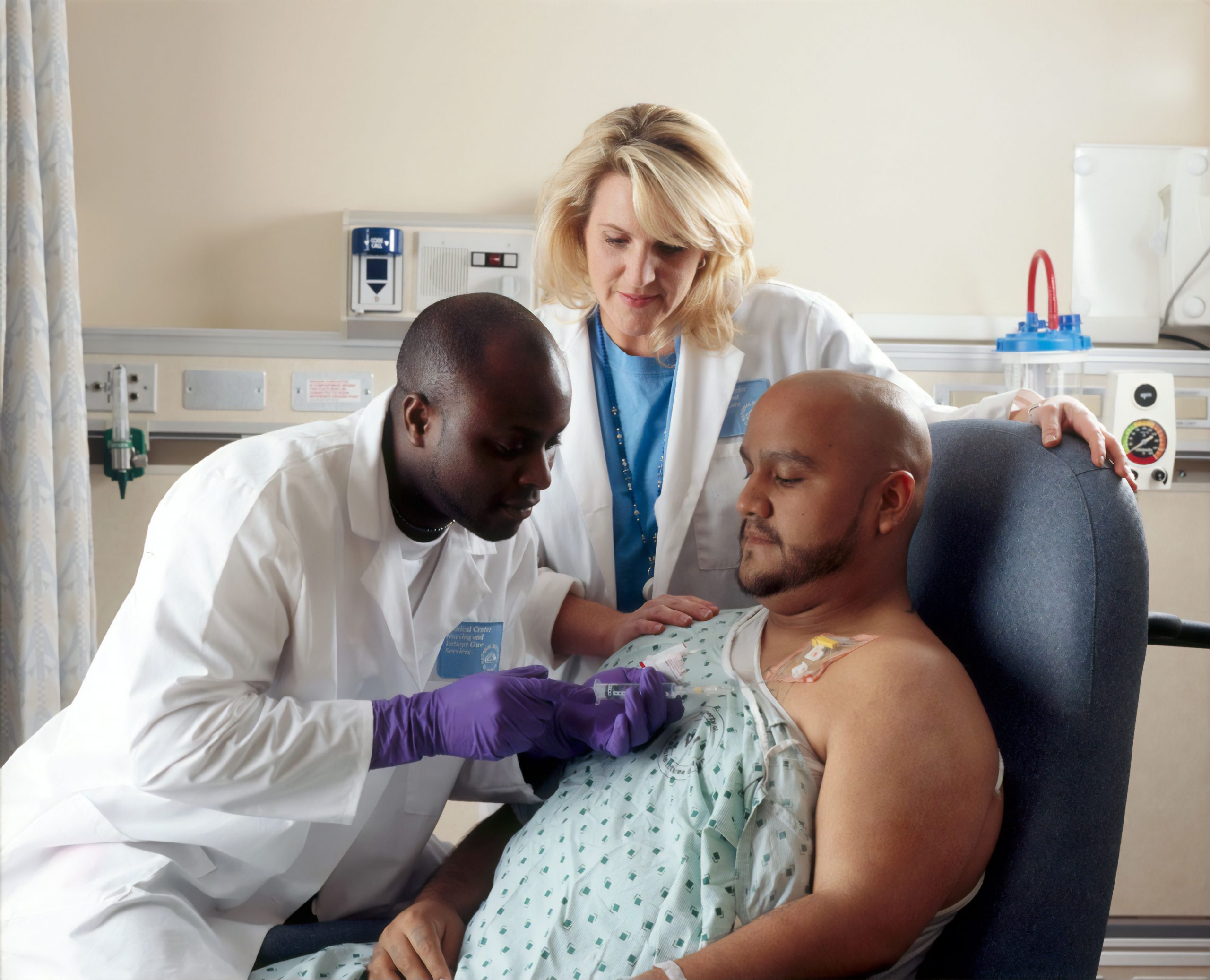 A Black doctor listens to a male patients chest while an assistant looks over his shoulder