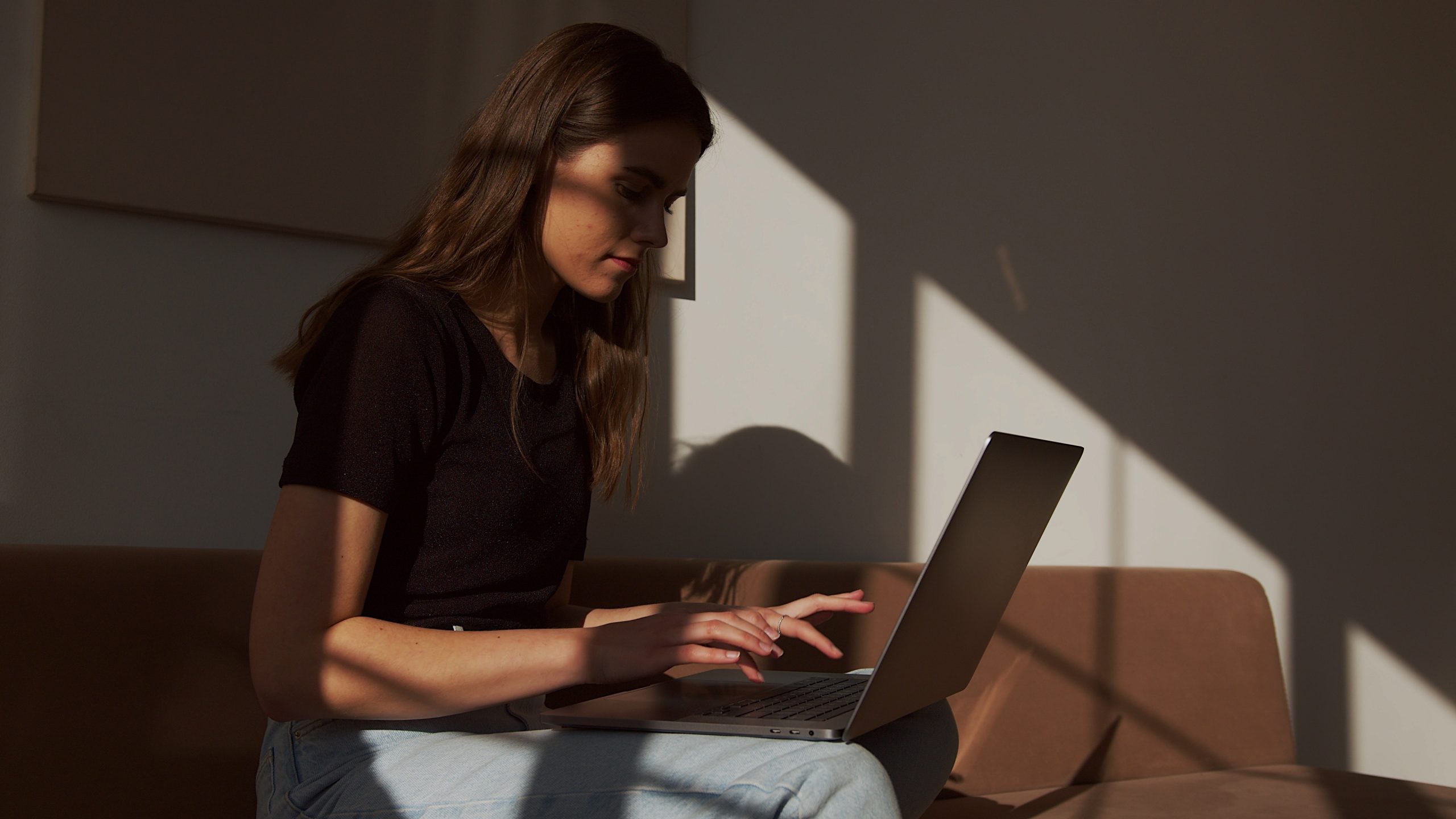 A young woman sits in the shadows while she searches on a laptop