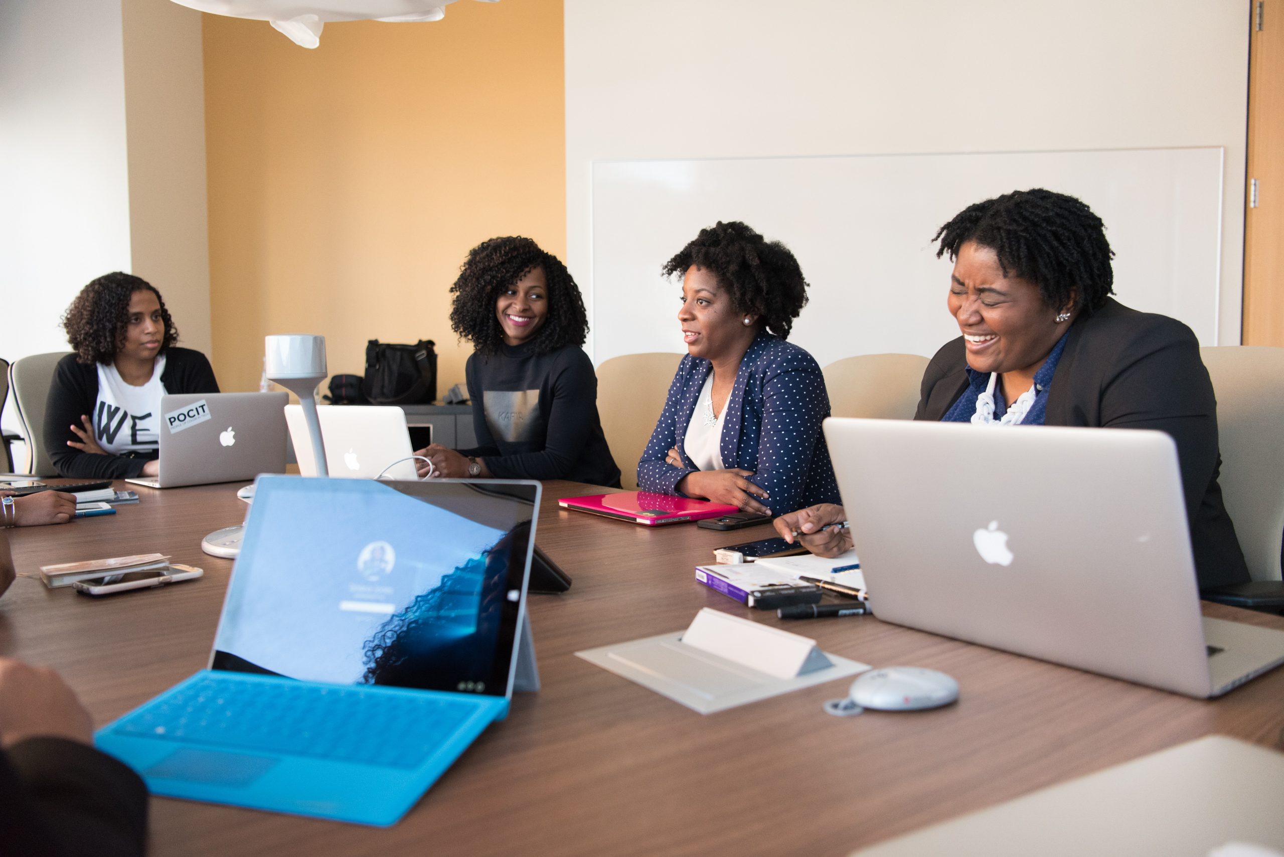 A group of Black women sit at a large office desk in a meeting