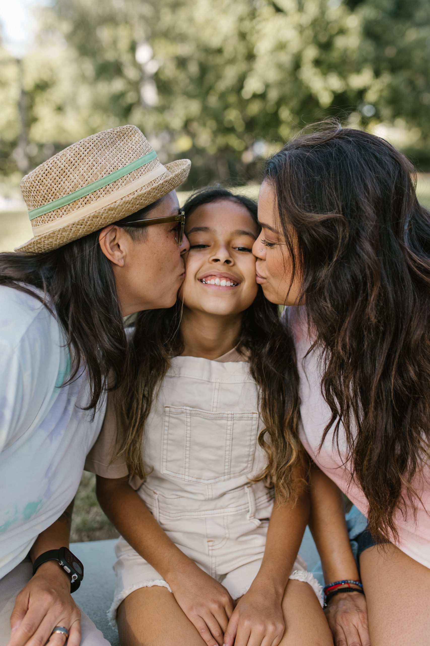 A lesbian couple kiss each of their daughter's cheeks