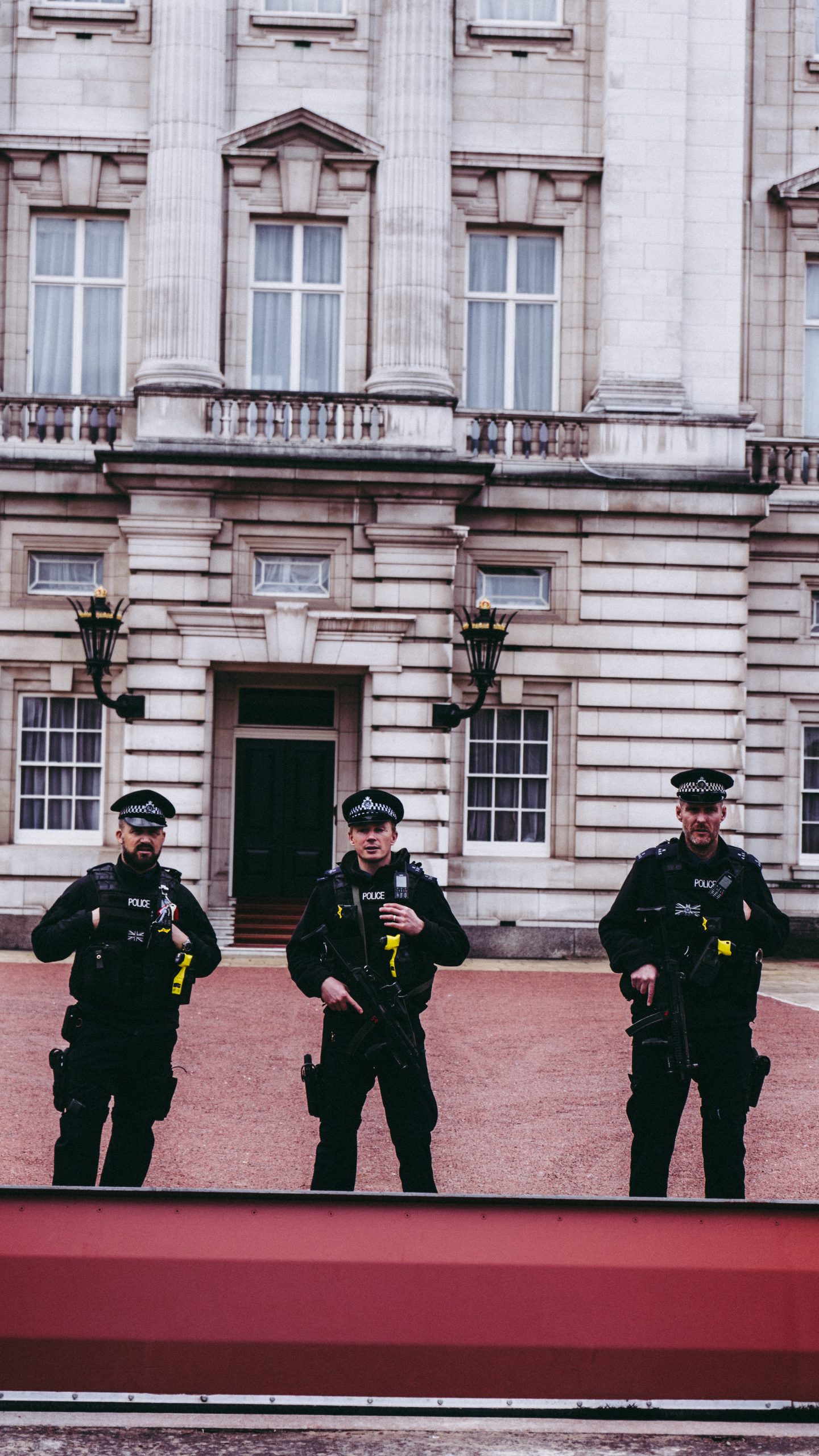 Three UK police officers stand outside a building in London. hey are armed and wear all black