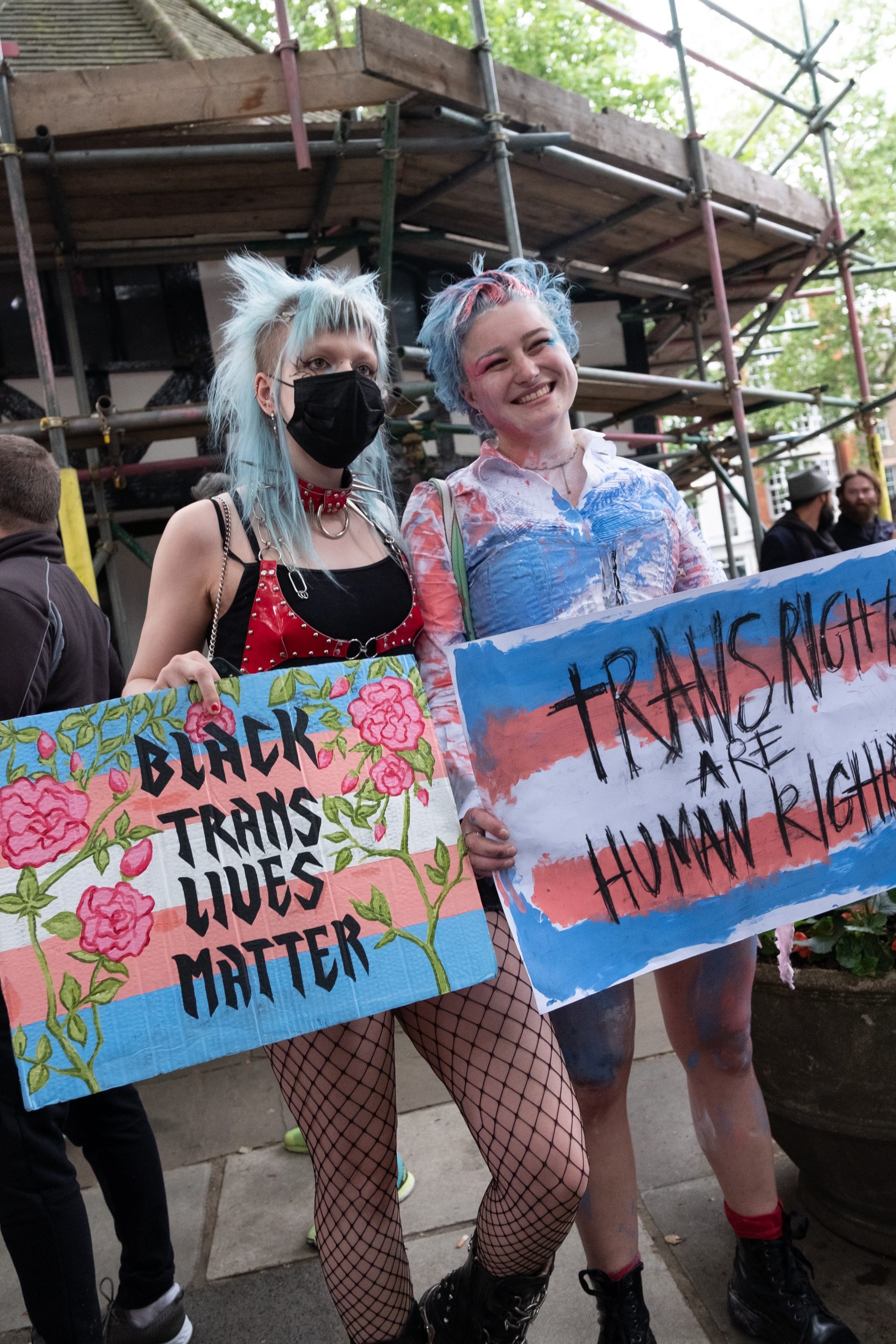 Two young people hold protest signs during a march. he one on the left reads "black trans lives matter" and the one on the left reads "trans rights are human rights"