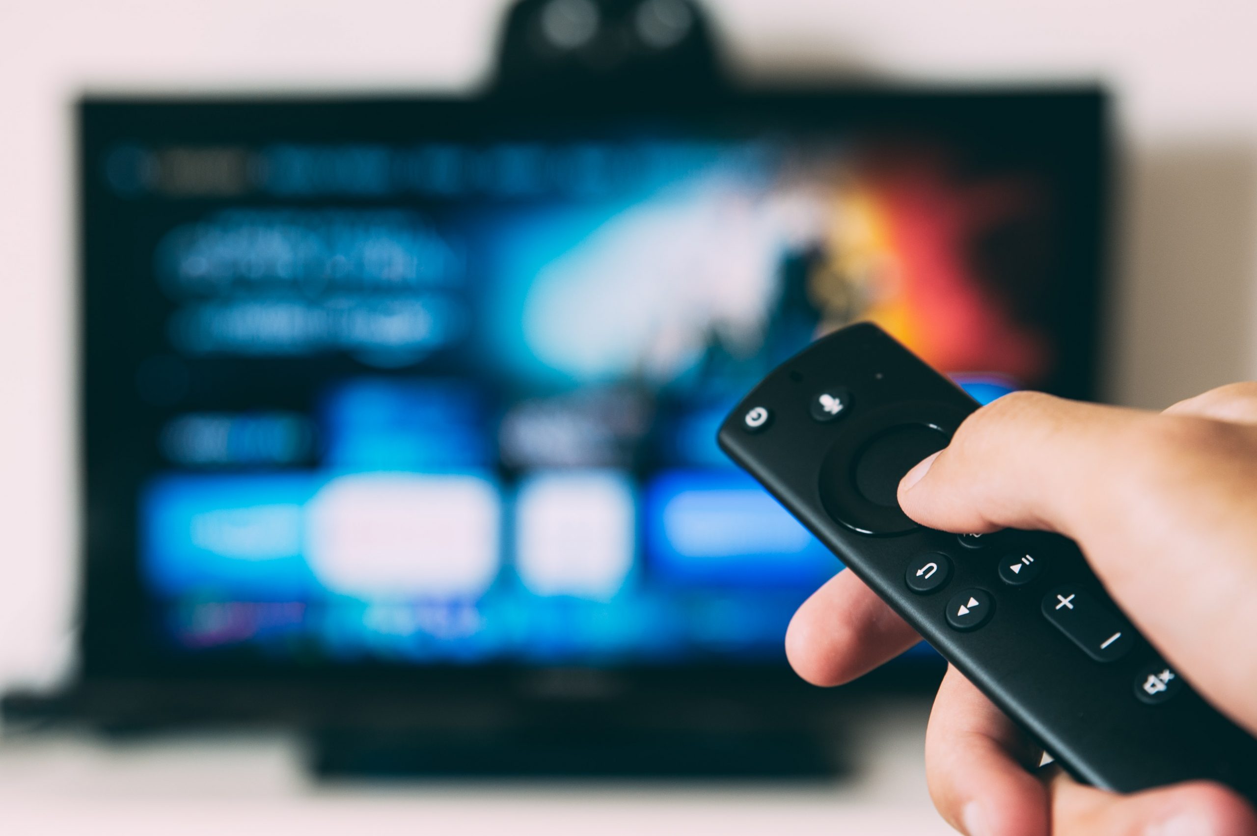 Person holding Amazon Fire TV remote and pointing it at blurry background of TV