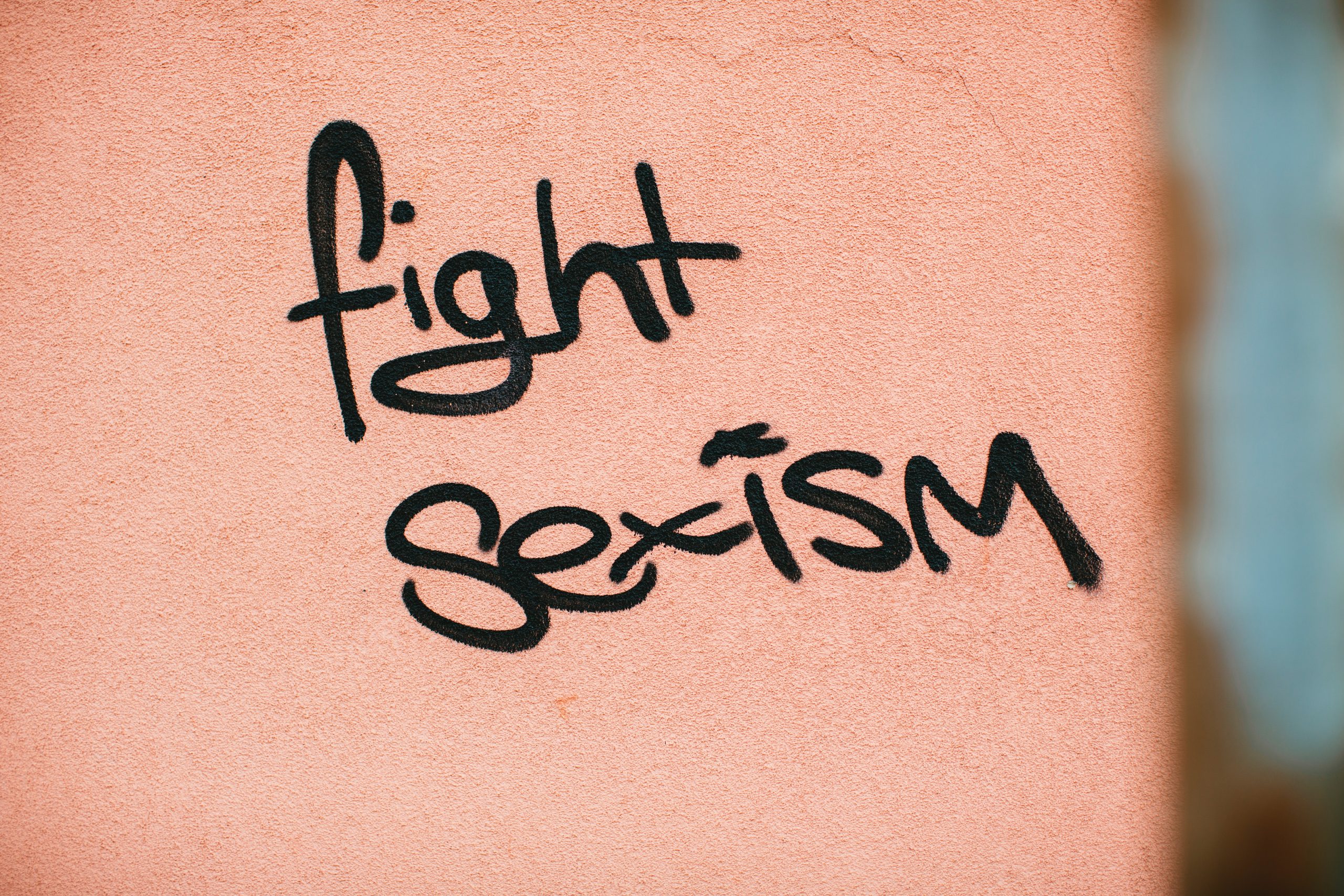 Graffiti reads "fight sexism" on a pink wall