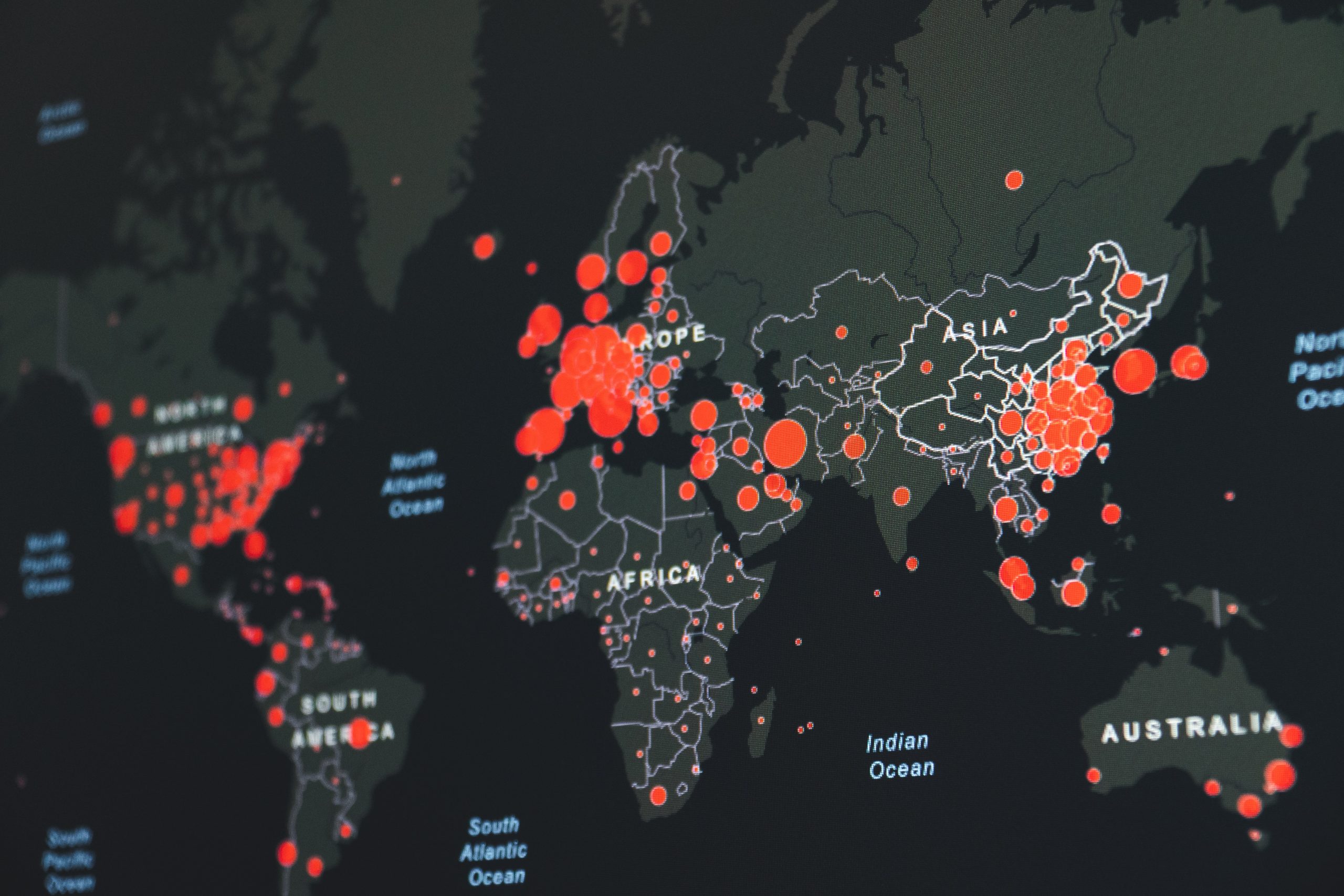 A digital map shows hotspots for Covid-19 infection rates across the globe. Hospots are highlighted with red dots and the map is in black and grey