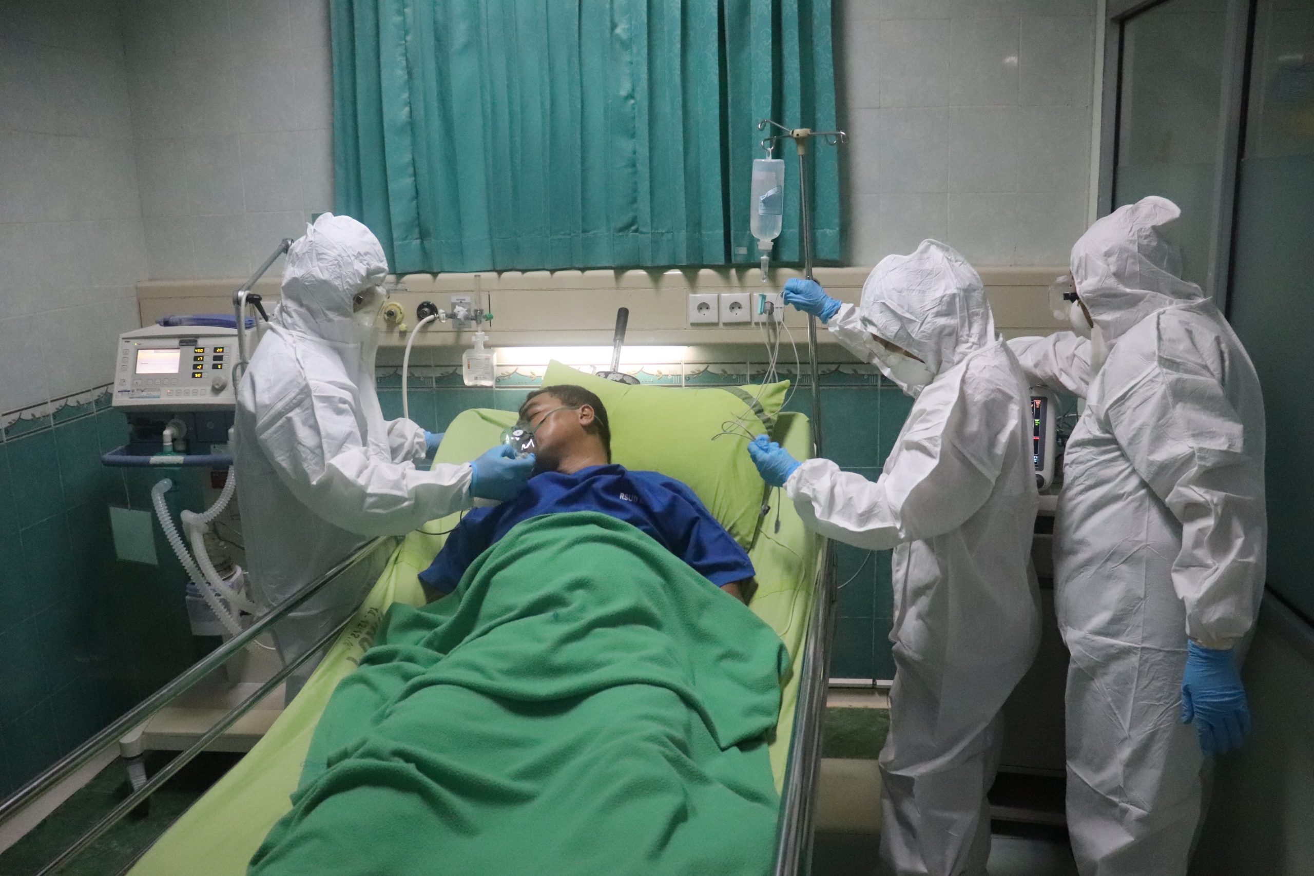 A man lies in a hospital bed surrrounded by medical workers in full protective suits.