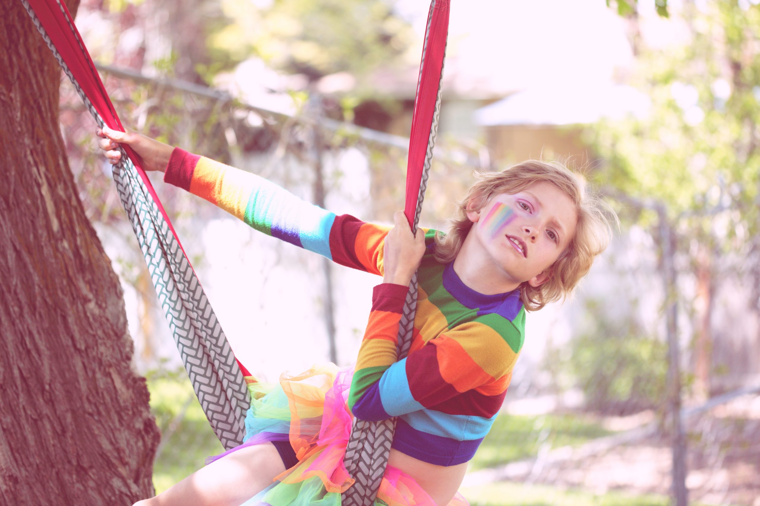 A young child dressed in rainbow colours with a trans pride flag on their cheek swings from a rope swing