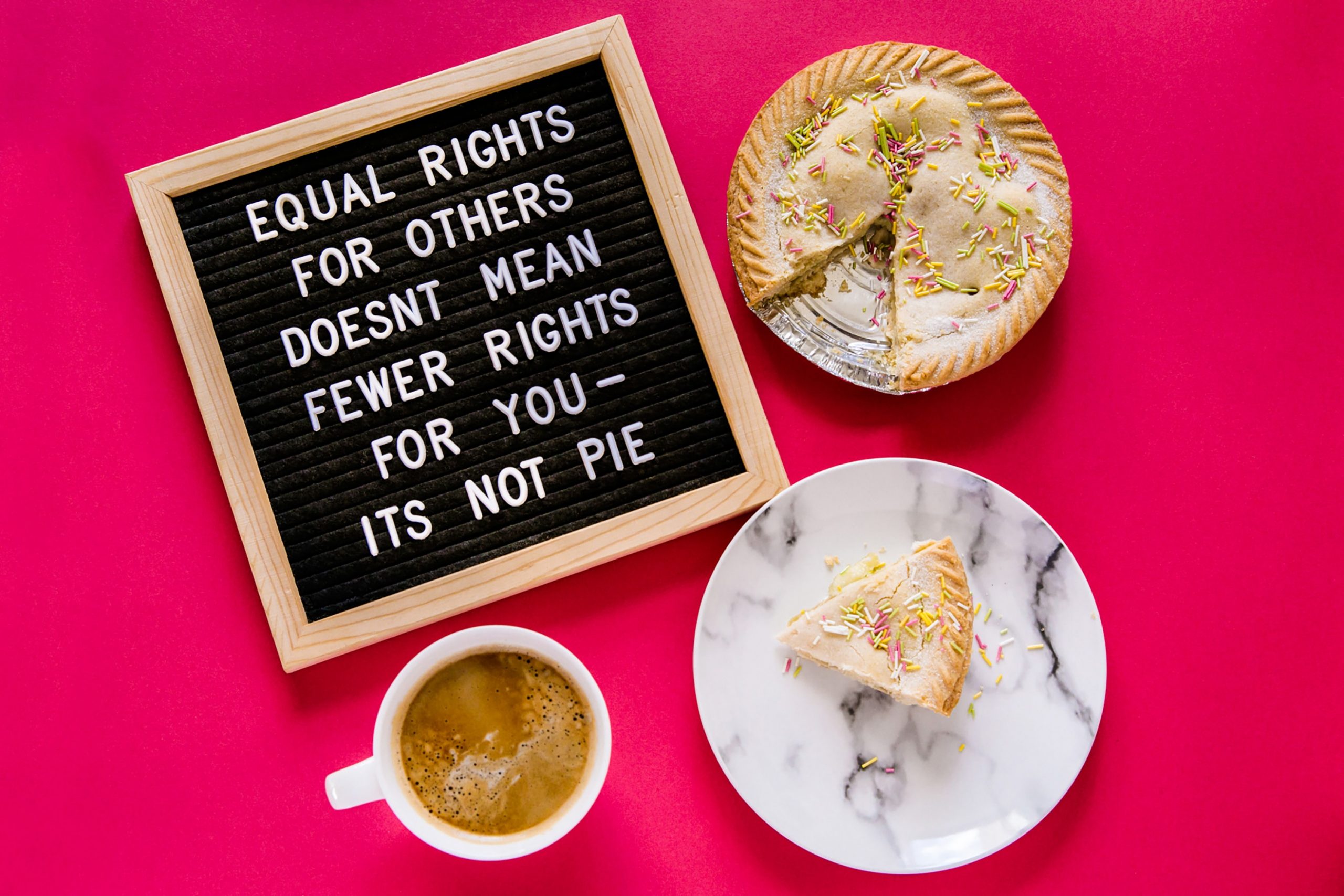 On a red background there is a spread of a coffee mug, a pie, and a plate with a slice of the pie on i. A blackboard lies next to it and reads "equal rights for others doesn't mean fewer rights for you. It's not pie.