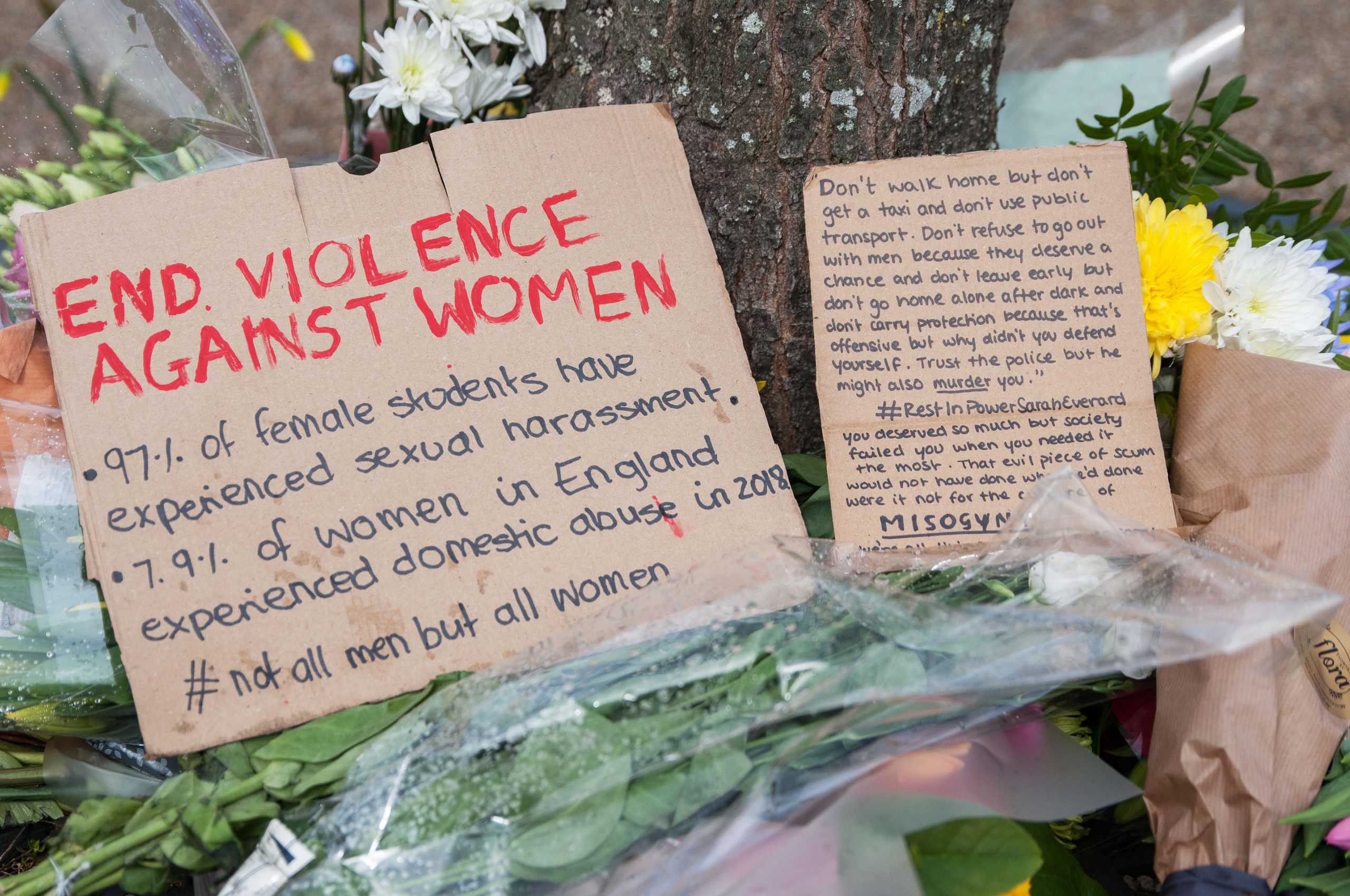 Flowers are laid to rest. A sign reads "End violence against women".