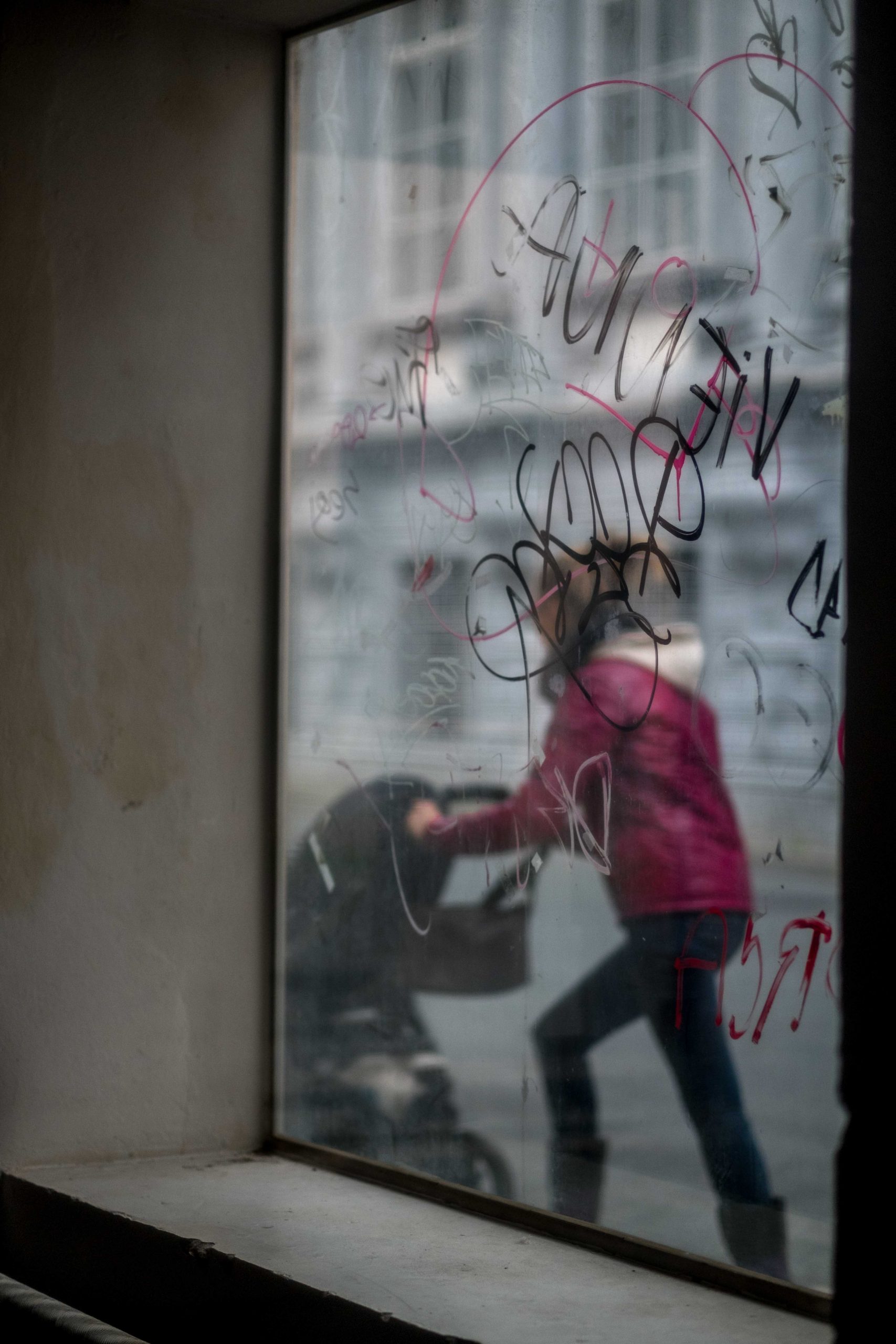 A woman can be seen pushesing a pram through a graffitied window