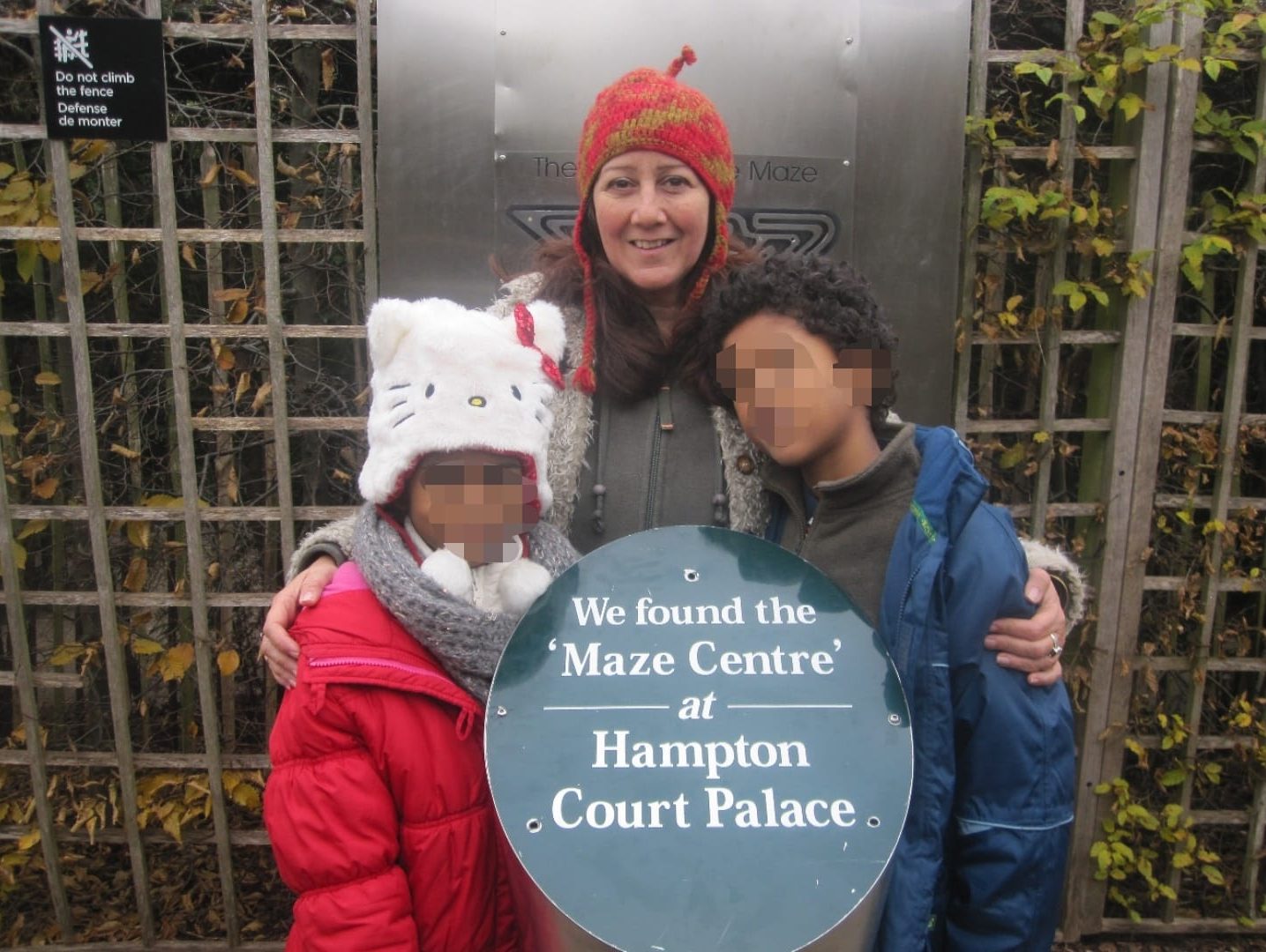 Anita Gera stands in front of a sign that reas 'Hampton court maze' with two children either side of her